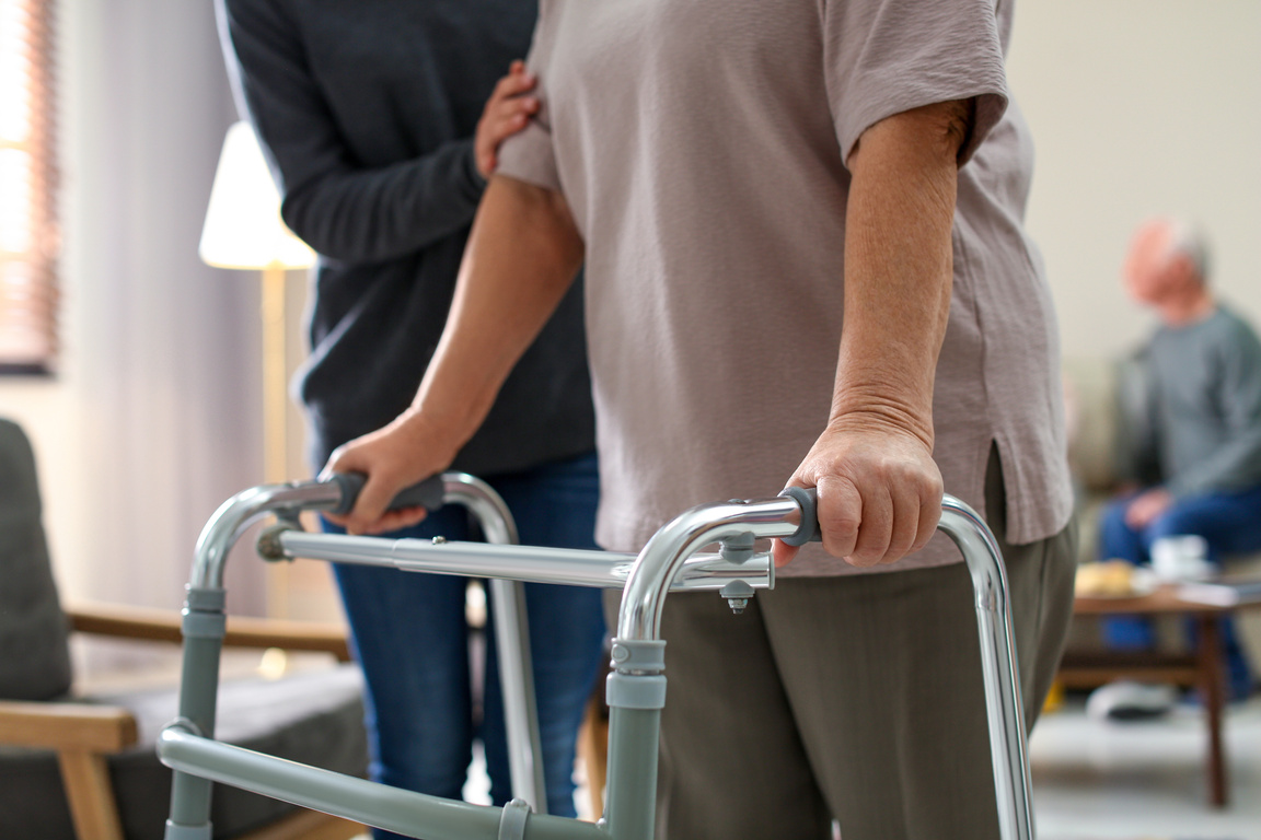 Care Worker Helping to Elderly Woman with Walker in Geriatric Ho